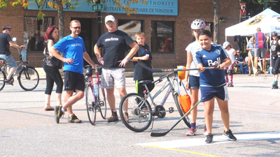 A group of people attending Open Streets Windsor 2017 stand near bikes while a boy plays street hockey
